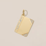 A gold rectangular pendant with a polished finish, featuring pavé-set clear stones along the left edge and bottom corners, shown on a light beige background.